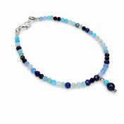 Handgefertigtes blaues Edelsteinarmband mit facettierten Perlen, silberfarbenem Karabinerverschluss und kleinem blauen Anhänger.