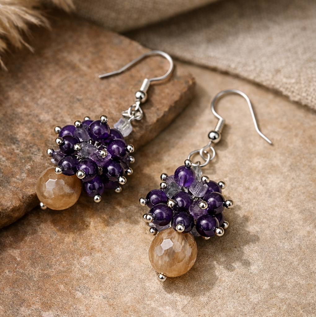 Handgemachte Edelstein-Ohrringe mit Mondstein, Amethyst und Fluorit auf warmem, natürlichem Untergrund, Detailfokus.