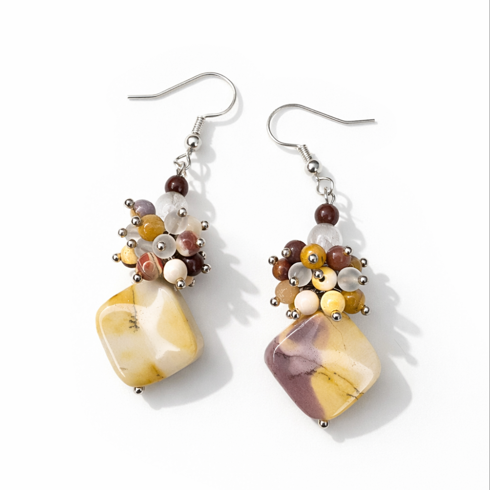 Handgemachte Ohrringe aus Mookait und Bergkristall auf weißem Hintergrund mit weichem Schatten.
