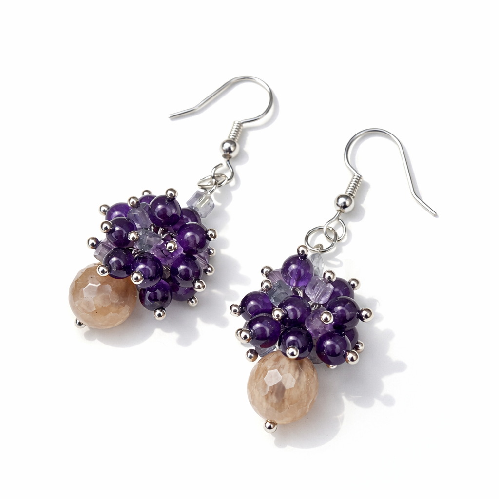 Zwei handgemachte Ohrringe aus Mondstein, Amethyst und Fluorit vor hellem Hintergrund mit weichem Schatten.